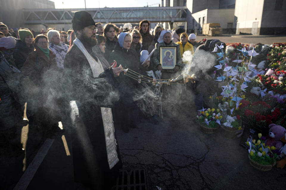 An Orthodox priest conducts a service at a makeshift memorial in front of the Crocus City Hall in the outskirts of Moscow, Russia, Monday, March 25, 2024. There were calls Monday for harsh punishment for those behind the attack on the Rossiya concert hall that killed more than 130 people as authorities combed the burnt-out ruins of the shopping and entertainment complex in search of more bodies. (AP Photo/Alexander Zemlyanichenko)