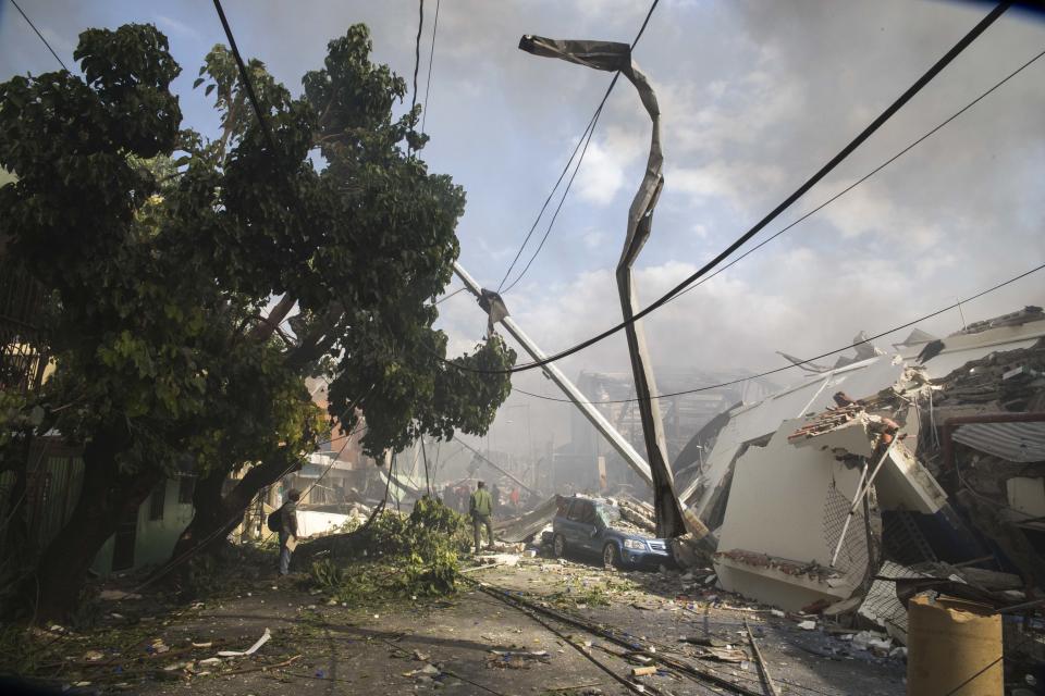 Residents watch first responders in the search and rescue efforts after an explosion at the Polyplas plant in the Villas Agricolas neighborhood in Santo Domingo, Dominican Republic, Wednesday, Dec. 5, 2018. The mayor told reporters the fire began when a boiler exploded early Wednesday afternoon at the plastics company. Authorities say at least two people have died. (AP Photo/Tatiana Fernandez)