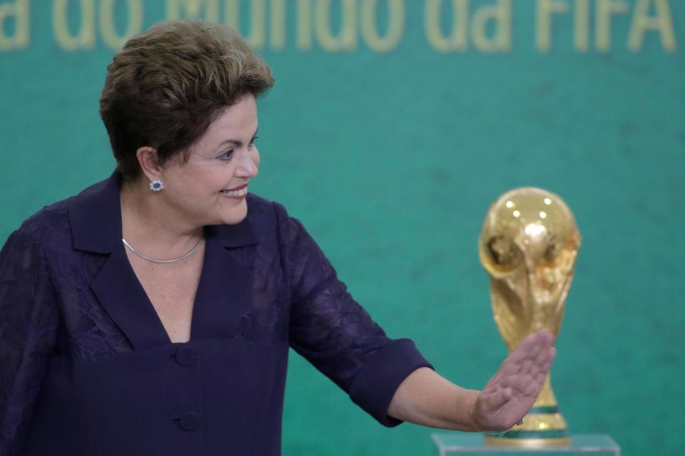 En esta fotografía del 2 de junio de 2014, la presidenta de Brasil Dilma Rousseff saluda a niños durante una ceremonia en la que el presidente de la FIFA Joseph Blatter presentó el trofeo de la Copa del Mundo en el palacio presidencial en Brasilia. (Foto AP/Eraldo Peres/Archivo)