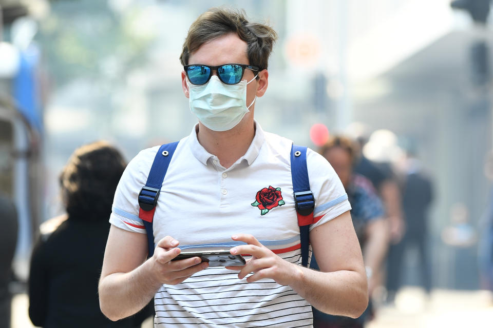 A man seen wearing a dust mask as smoke haze from bushfires in New South Wales blankets the CBD in Sydney, Tuesday, December 3, 2019. (AAP Image/Joel Carrett) NO ARCHIVING