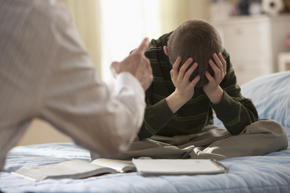 A parent yells and points at their child, who lowers their head in their hands and is distressed