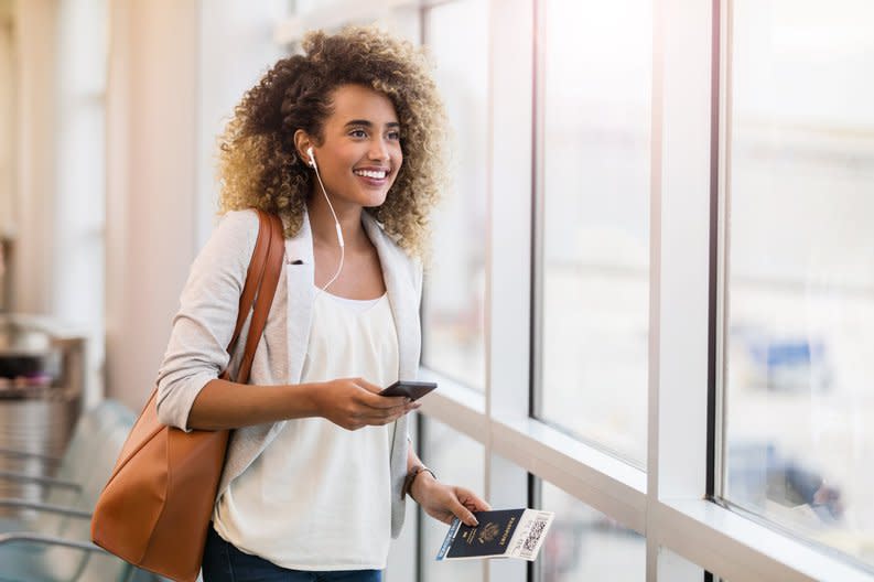 A woman smiling in an airport with her suitcase and passport.