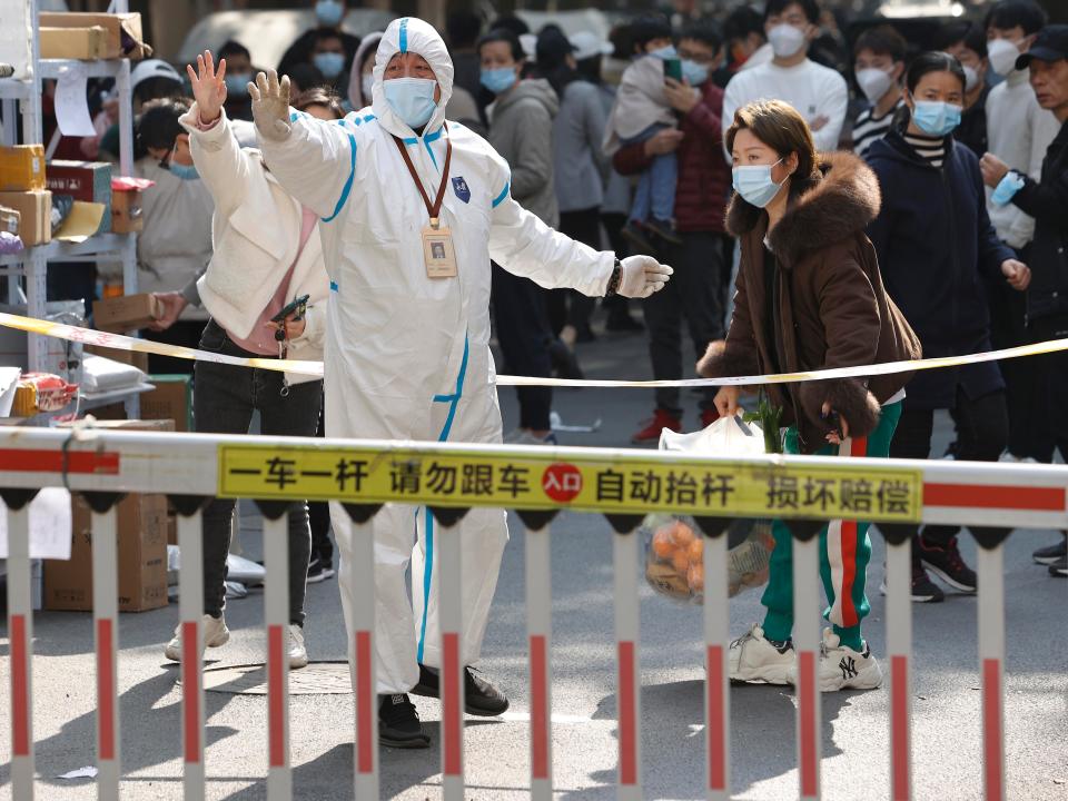A volunteer wearing PPE raises their hand at a residential gate.