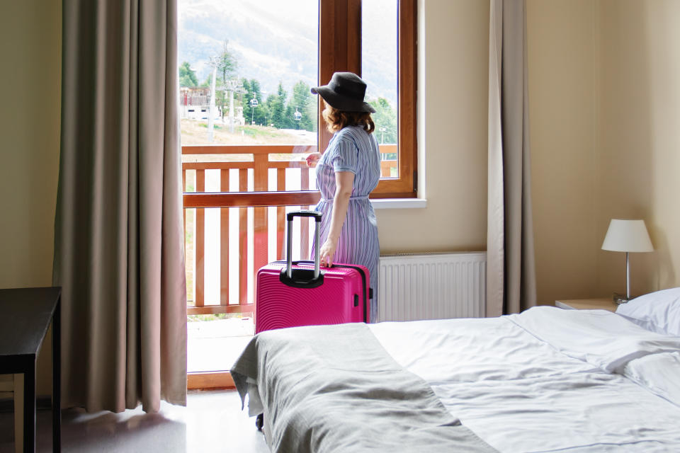 hotel room with mountain view, a tourist with a suitcase at the window of the apartment looks at the nature landscape