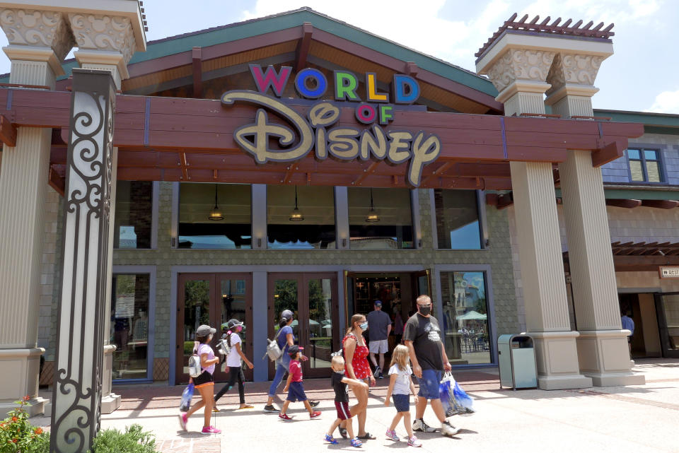 Shoppers wearing masks because of the coronavirus pandemic stroll by the World of Disney store at the Disney Springs shopping, dining and entertainment complex Tuesday, June 16, 2020, in Lake Buena Vista, Fla. Walt Disney World Resort theme parks plan to reopen on July 11. (AP Photo/John Raoux)