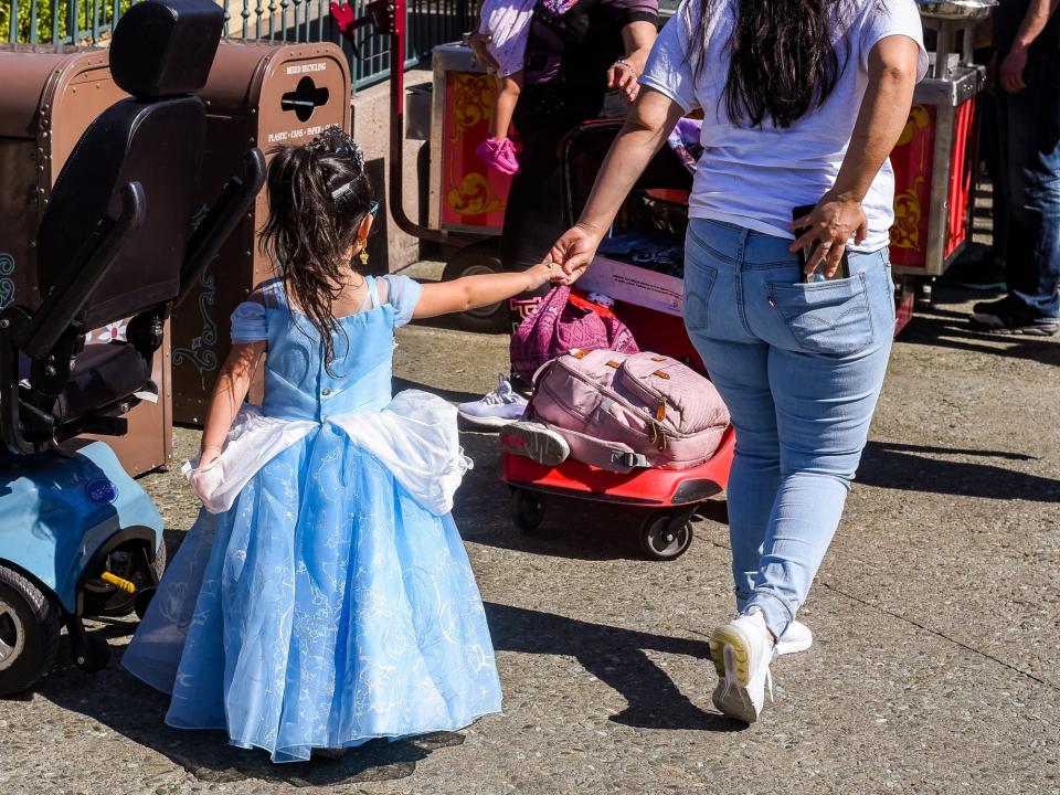 girl wearing a cinderella costume and holding an adult's hand at disneyland