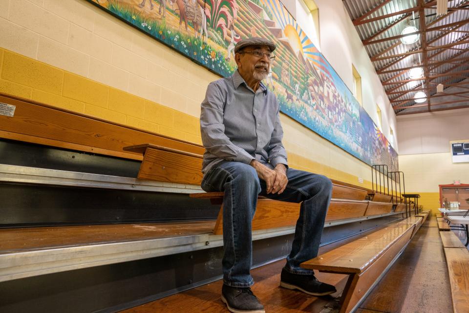 Andy Valdivia sits in front of his mural "Village To Village" on Friday in the gymnasium of  the Marlo Cuevas Balandran Activity Center at Our Lady of Guadalupe Church.