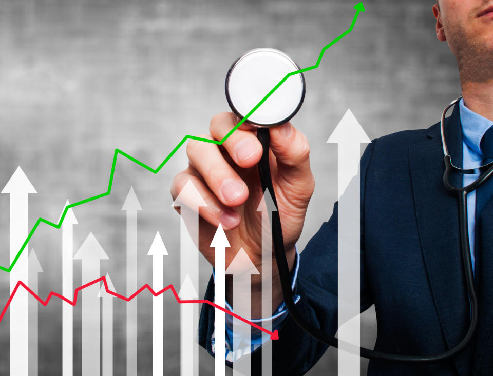 Hand holding a stethoscope to a line chart trending upward