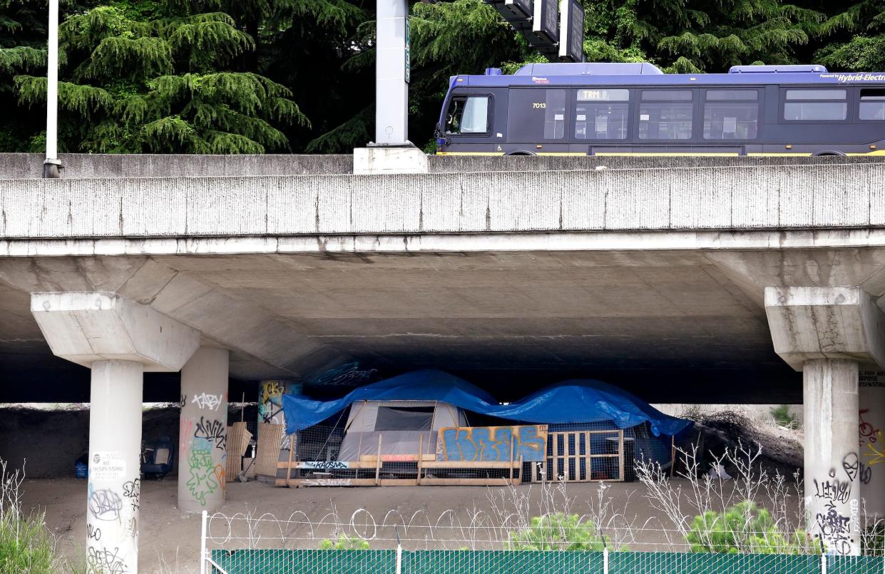 A bus passes overhead on Interstate 5 in Seattle as a shelter of tents, tarps and wood sits below in May 2016.
