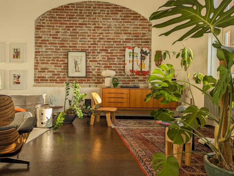 white living room with one exposed brick wall, lots of plants, and mid century modern furniture