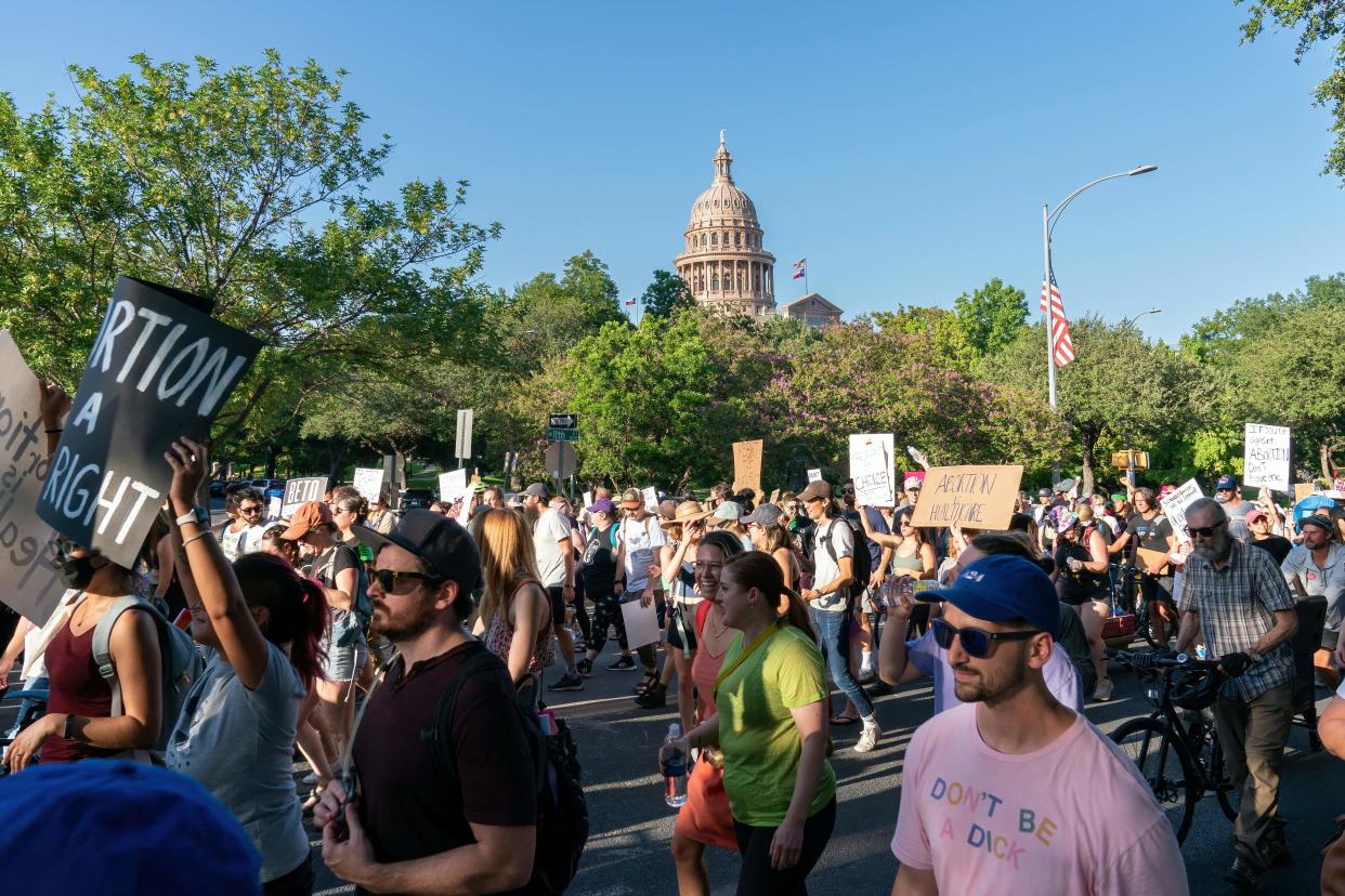 A man wearing a pink T-shirt saying Don't be a d*** marches alongside people carrying signs saying things like: Abortion is a right and Abortion is health care.