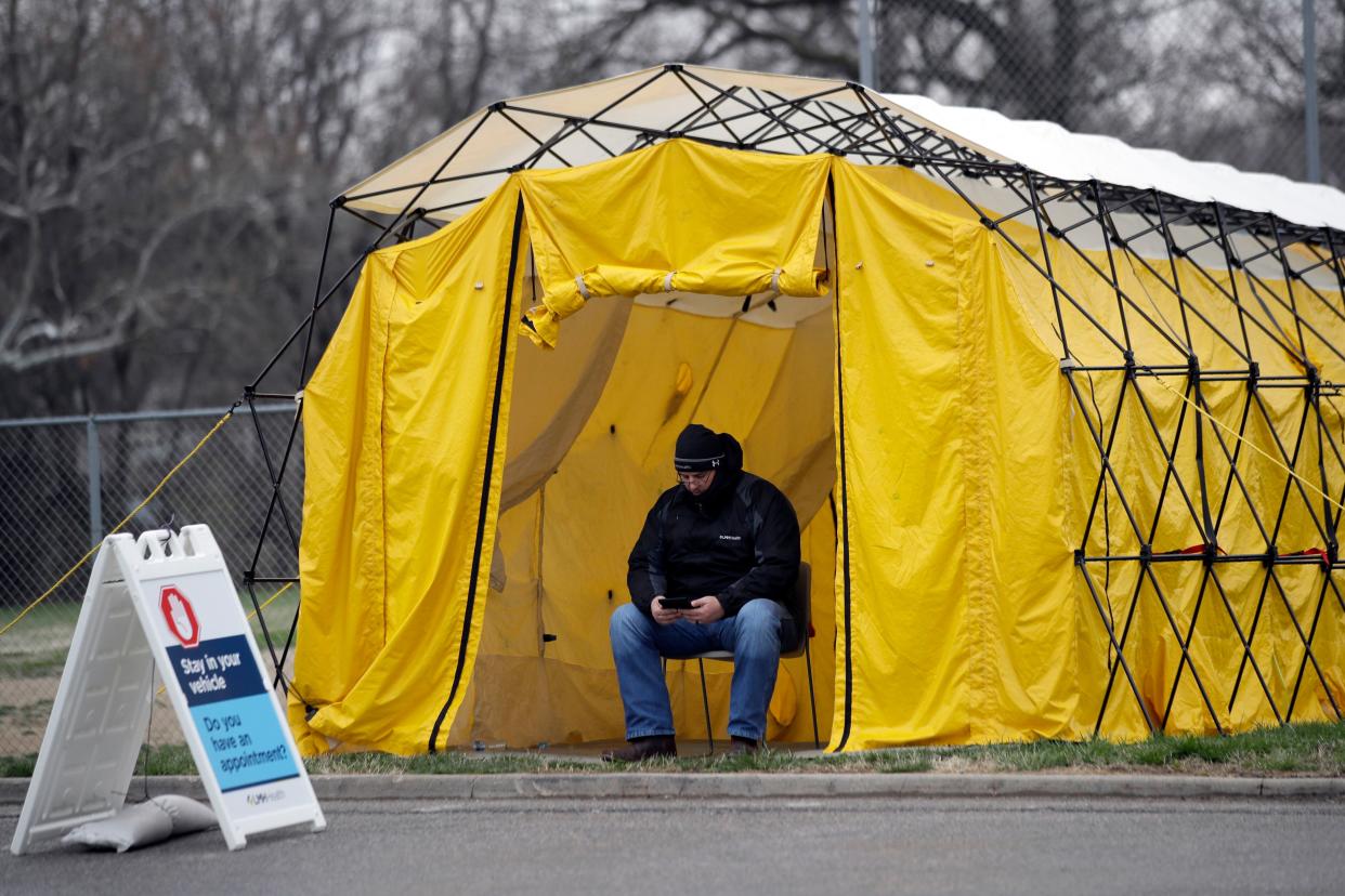 A hospital worker checks messages while waiting at the entrance of a by appointment only drive-thru coronavirus testing location at Lawrence Memorial Hospital in Lawrence, Kan., Tuesday, March 24, 2020.