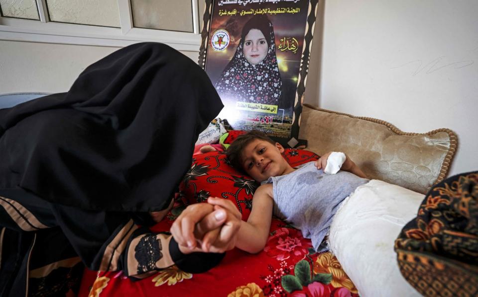 Palestinian mother Rasha Qadoom sits by her wounded child Rayed near a poster depicting her five-year-old daughter Alaa, who was killed during the latest conflict - MAHMUD HAMS/AFP