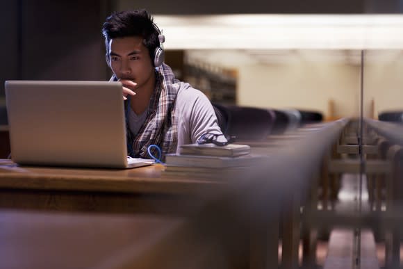 A person sitting at a desk, wearing headphones, and working on a laptop.
