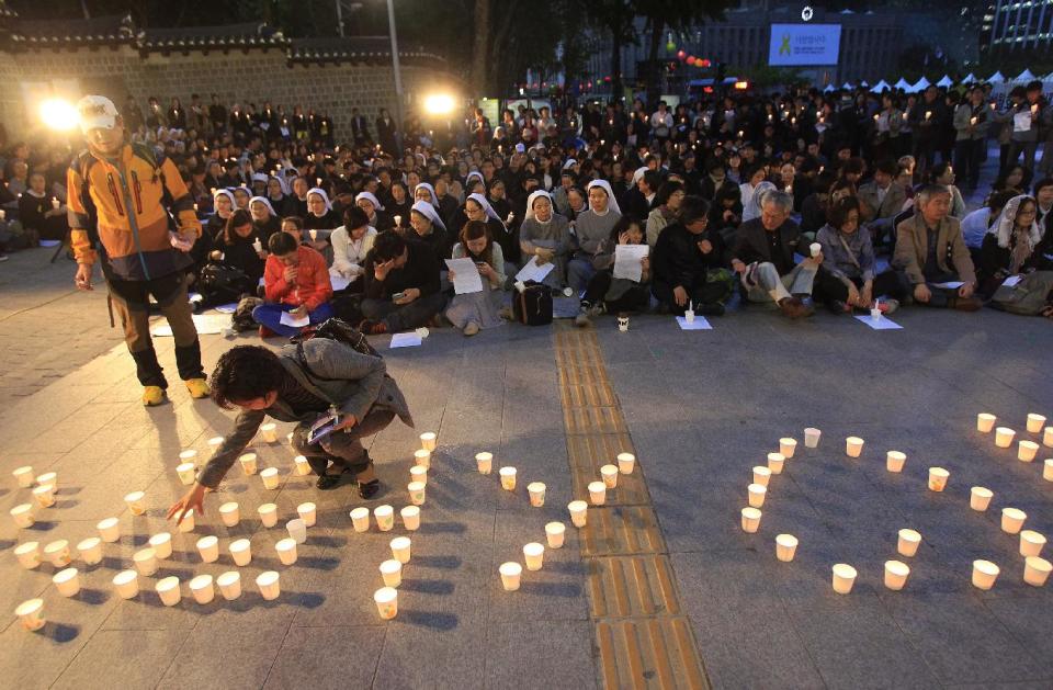 A woman places a candle to form a word of "Love" during a service, paying tribute to the victims of the sunken ferry Sewol in Seoul, South Korea, Wednesday, April 30, 2014. Two weeks after the ferry sank off South Korea's southern cost, divers have recovered over 200 bodies from the wreckage, but they fought strong currents and floating debris inside the ship Wednesday as they searched for 90 passengers still missing. (AP Photo/Ahn Young-joon)