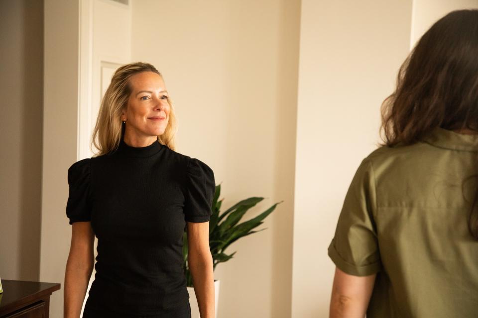 A woman in a black top walks towards the camera, looking out towards another woman walking away from the camera.