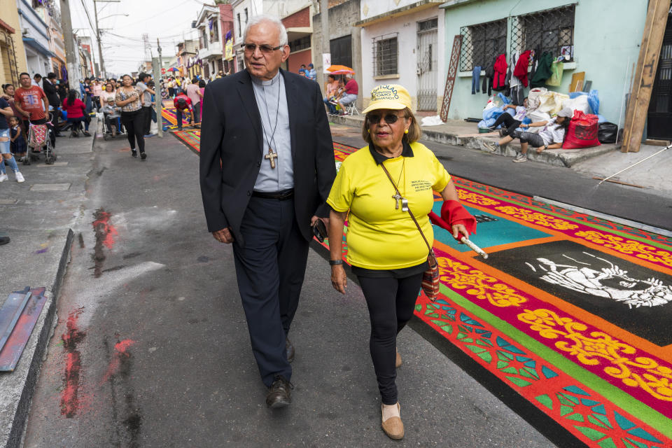 Cardinal Alvaro Ramazzini and a Catholic volunteer walk past a sawdust carpet in Guatemala City, Saturday, March 23, 2024. Elevated by Pope Francis in 2019 to the top hierarchy of the Catholic Church, Ramazzini has continued his focus on the poor, the Indigenous and the migrant. (AP Photo/Moises Castillo)