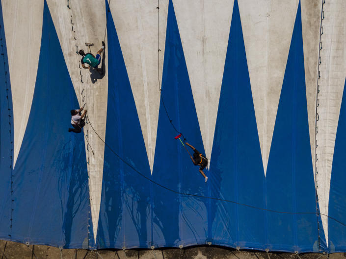 Bastian Rubio, second left, and workers wash a portion of the Timoteo Circus tent, on the outskirts of Santiago, Chile, Thursday, Dec. 15, 2022. An adopted grandson of founder René Valdés, Rubio is in charge of washing the circus tent, as well as setting it up and taking it down and performs as a musician, juggler, tightrope walker and clown. (AP Photo/Esteban Felix)