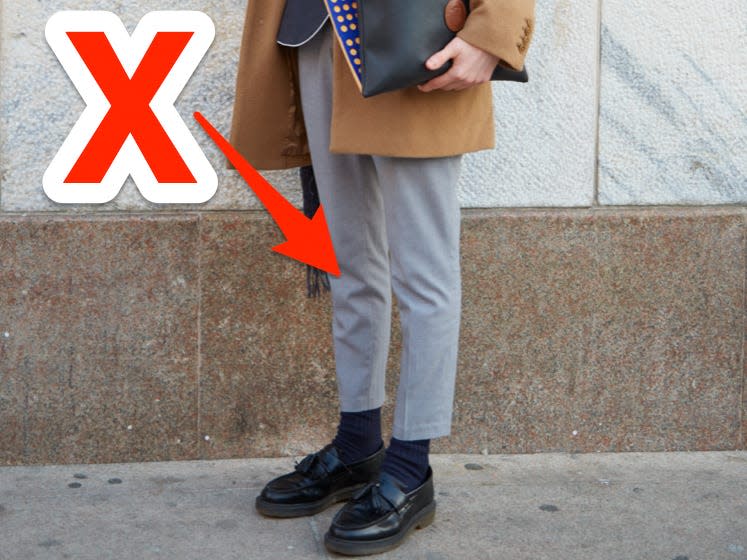 red x and arrow pointing at someone wearing skinny gray trousers with a camel coat and black loafers