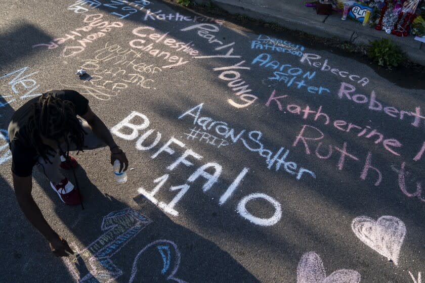 BUFFALO, NY - MAY 15: Aaron Jordan, of Buffalo, adds to a sidewalk chalk mural depicting the names of the people killed yesterday as people gather at the scene of a mass shooting at Tops Friendly Market at Jefferson Avenue and Riley Street on Sunday, May 15, 2022 in Buffalo, NY. The fatal shooting of 10 people at a grocery store in a historically Black neighborhood of Buffalo by a young white gunman is being investigated as a hate crime and an act of "racially motivated violent extremism," according to federal officials. (Kent Nishimura / Los Angeles Times)