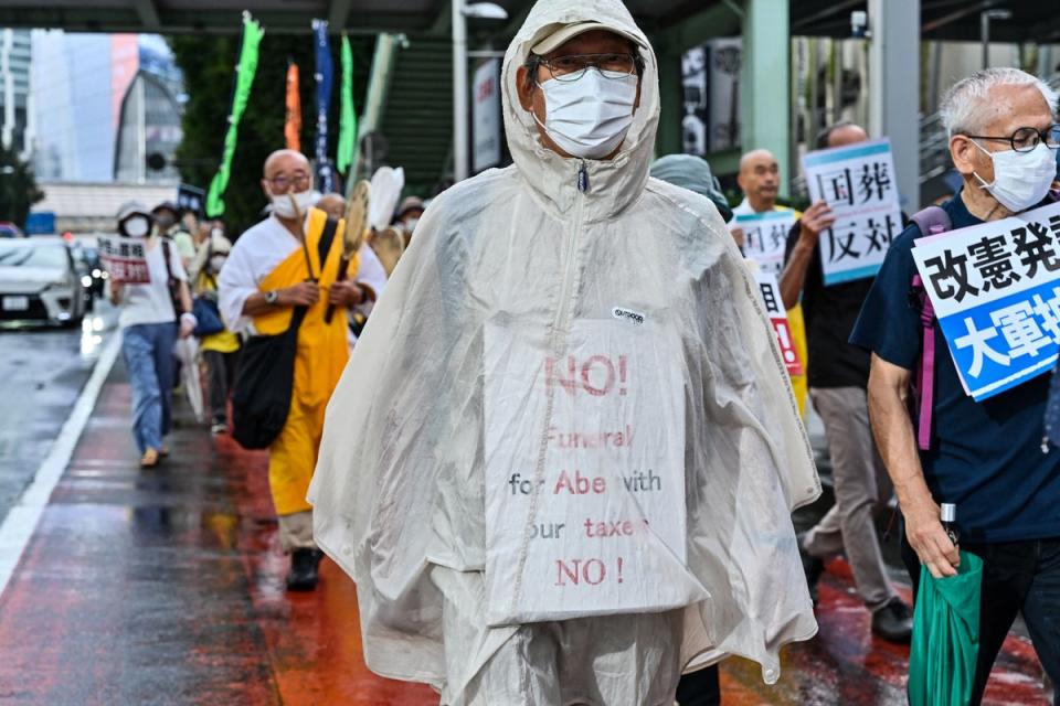 A man wrapped in a rain poncho with an anti-Abe placard takes part in a march with anti-war, anti-nuclear and other protesters against the government’s funding for the funeral of Shinzo Abe (AFP via Getty Images)