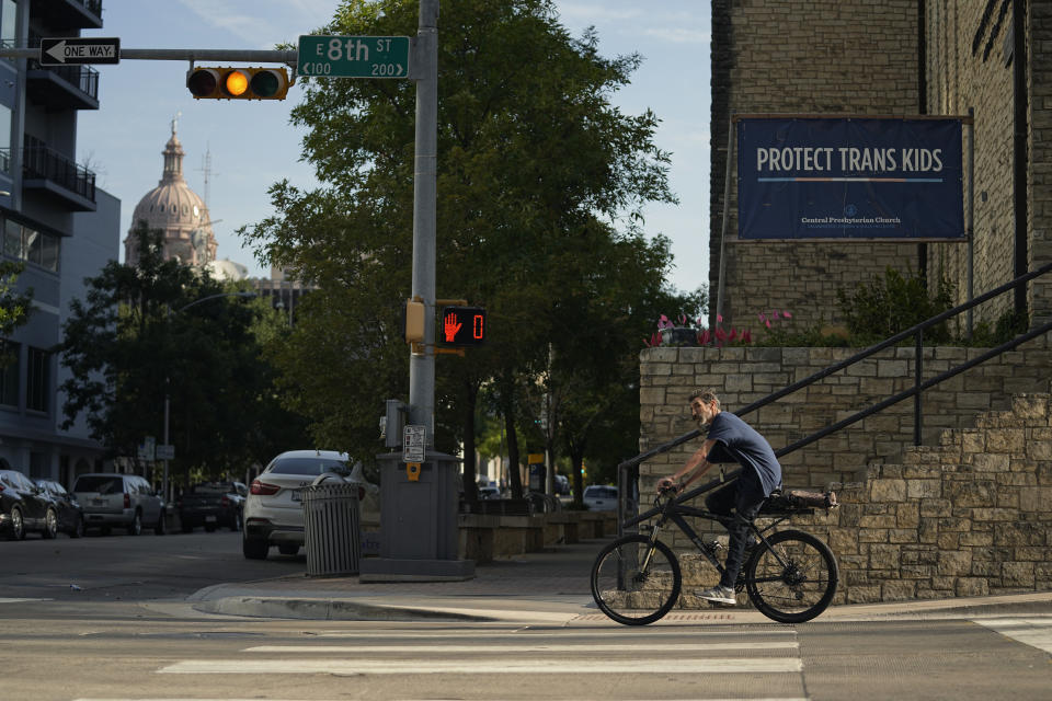 A cyclist passes a sign encouraging the protection of transgender children at Central Presbyterian Church near the Texas Capitol, Tuesday, Aug. 15, 2023, in Austin, Texas. Waiting lists for gender-affirming health care are growing in states that declared themselves refuges for transgender people as bans for such care for minors take effect around the country. Texas, one of the largest states, has a ban that's set to take effect Sept. 1. (AP Photo/Eric Gay)