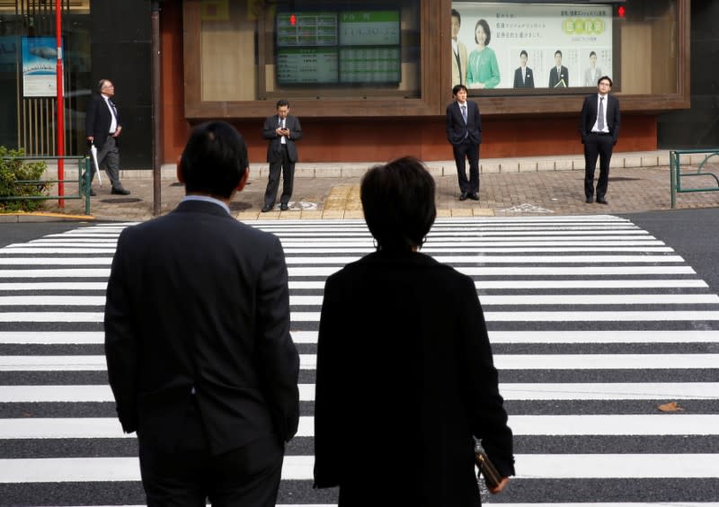 Pedestrians stand in front of an electronic board showing stock and foreign currency markets information outside a brokerage in Tokyo, Japan, December 1, 2016. REUTERS/Kim Kyung-Hoon