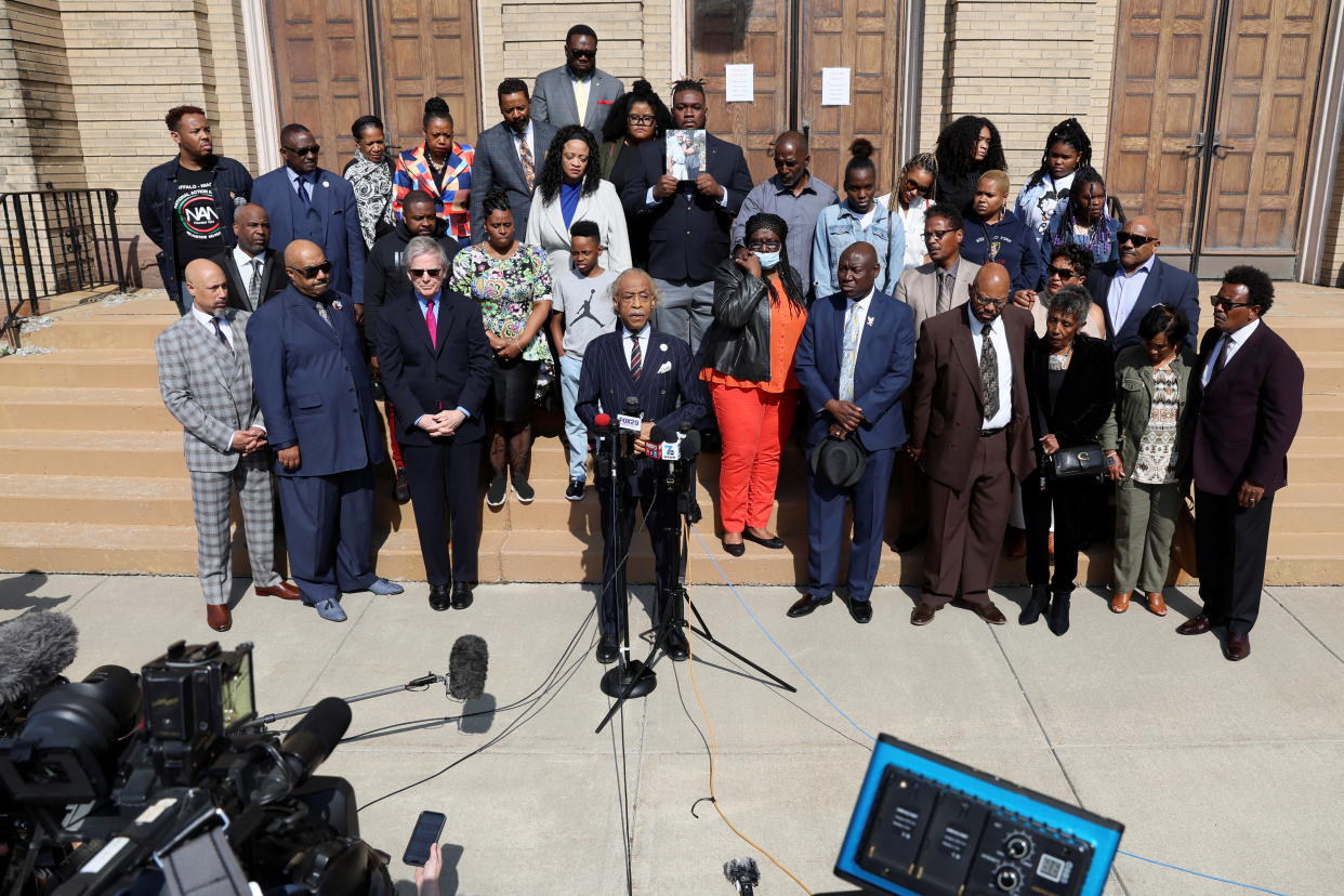 The Reverend Al Sharpton, flanked by relatives of some of the Buffalo shooting victims, speaks into a microphone.