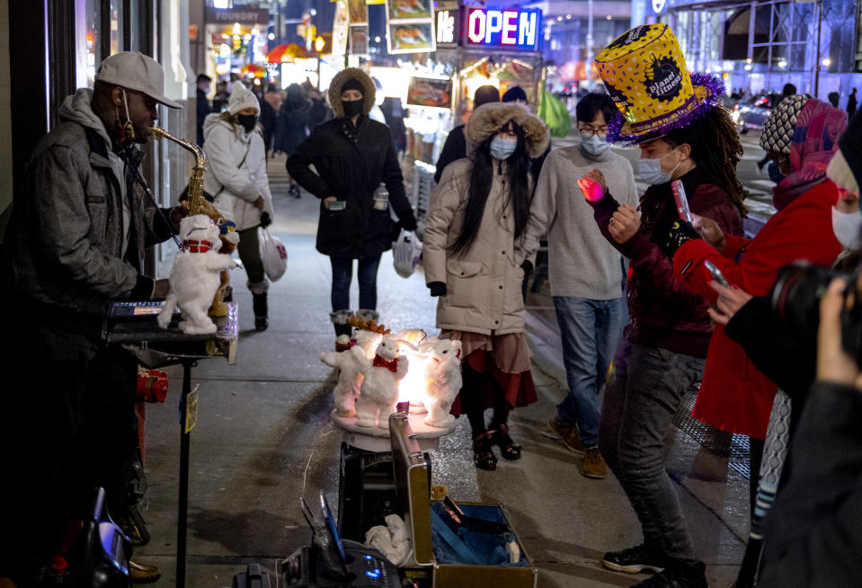 Pedestrians pass by and also watch street entertainment on Eighth Avenue, adjacent to a closed-off Times Square in New York, late Thursday, Dec. 31, 2020, as celebrations have been truncated this New Year's Eve due to the ongoing pandemic. (AP Photo/Craig Ruttle)