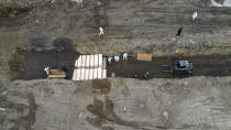 Workers wearing personal protective equipment bury bodies in a trench on Hart Island, Thursday, April 9, 2020, in the Bronx borough of New York. On Thursday, New York City’s medical examiner confirmed that the city has shortened the amount of time it will hold on to remains to 14 days from 30 days before they will be transferred for temporary internment at a City Cemetery. Earlier in the week, Mayor Bill DeBlasio said that officials have explored the possibility of temporary burials on Hart Island, a strip of land in Long Island Sound that has long served as the city’s potter’s field. (AP Photo/John Minchillo)