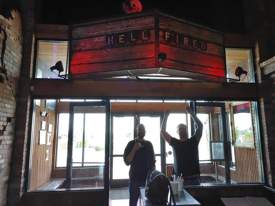 Chad Diaz, owner and operator of Hellfired Pizza, cheers under a new sign at the former Rock Wood Fired Pizza restaurant in Kennewick with Jason Door, general manager.