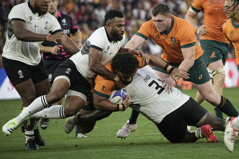 Australia's Zane Nonggorr, center, is tackled by Fiji's Luke Tagi during the Rugby World Cup Pool C match between Australia and Fiji at the Stade Geoffroy Guichard in Saint-Etienne, France, Sunday, Sept. 17, 2023. (AP Photo/Laurent Cipriani)