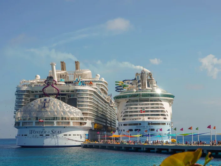Two cruise ships docked at CocoCay on a partly-cloudy day with blue skies