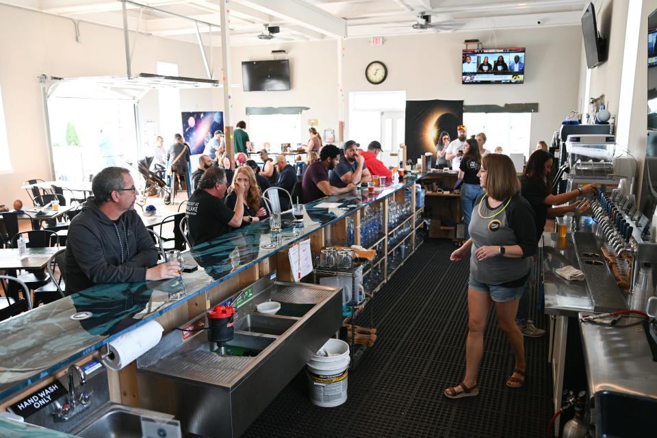 Patrons at Indian Lake Brewing Company in Russel's Point ordered astronomy-themed brews at a total solar eclipse party on April 8, 2024. Co-owner Rebekah Smith, right, said she was worried people might not show up because of tornado damage in the area, but she said the bar has been busy all weekend.