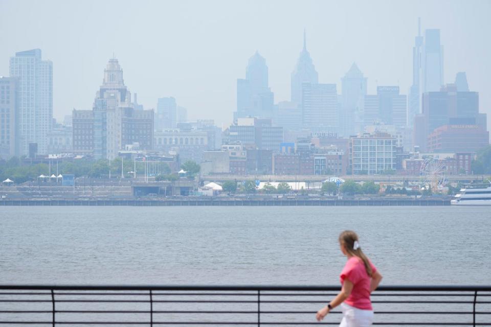 A person walks in Camden, N.J., in view of the hazy Philadelphia skyline, Wednesday, June 7, 2023. Intense Canadian wildfires are blanketing the northeastern U.S. in a dystopian haze, turning the air acrid, the sky yellowish gray and prompting warnings for vulnerable populations to stay inside. (AP Photo/Matt Rourke)