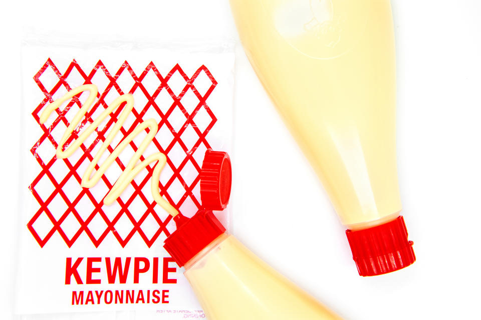 Two bottles of Kewpie mayonnaise lying diagonally with caps facing down, on white background near the red logo