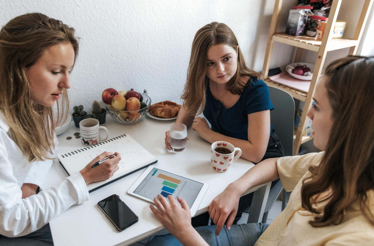 three young woman discussing about stats on digital tablet at kitchen table