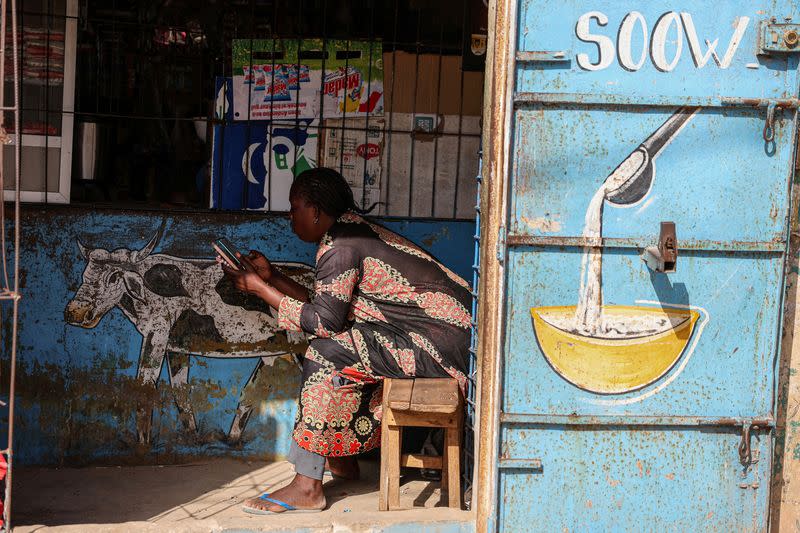 FILE PHOTO: A woman uses her mobile phone as she waits for a customer at her family shop in Bargny, on the outskirts of Dakar