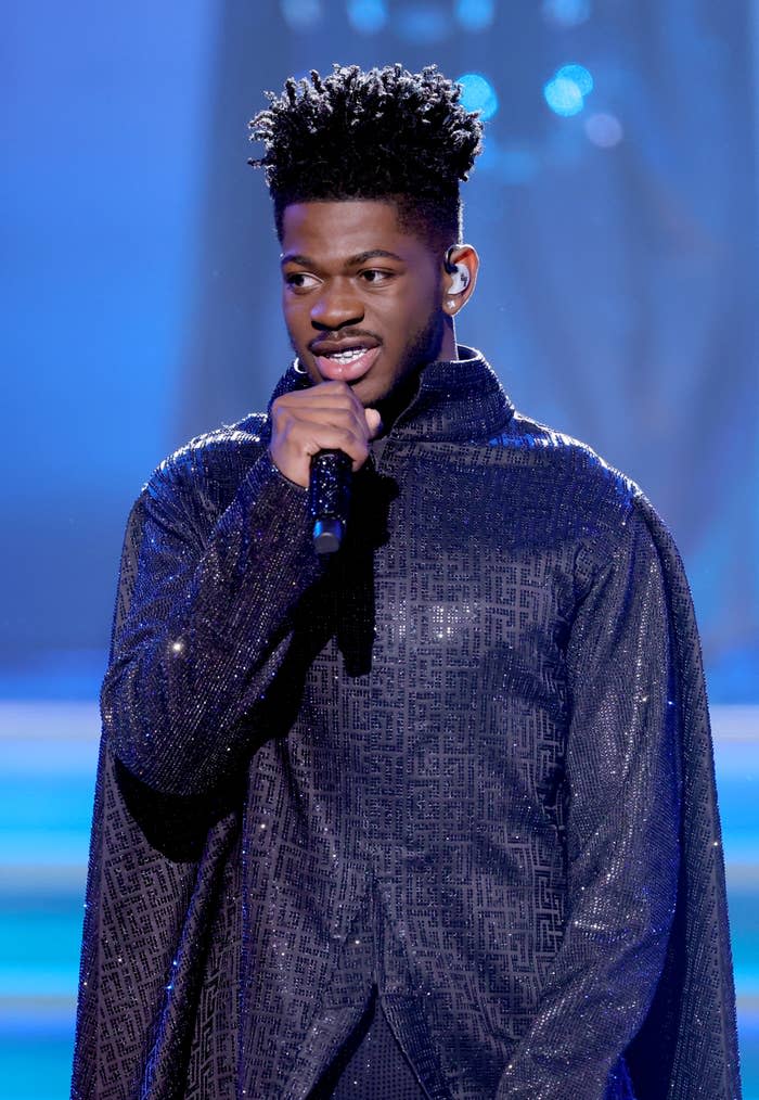 Lil Nas X performs on stage, wearing a sparkling, high-neck cloak-style outfit