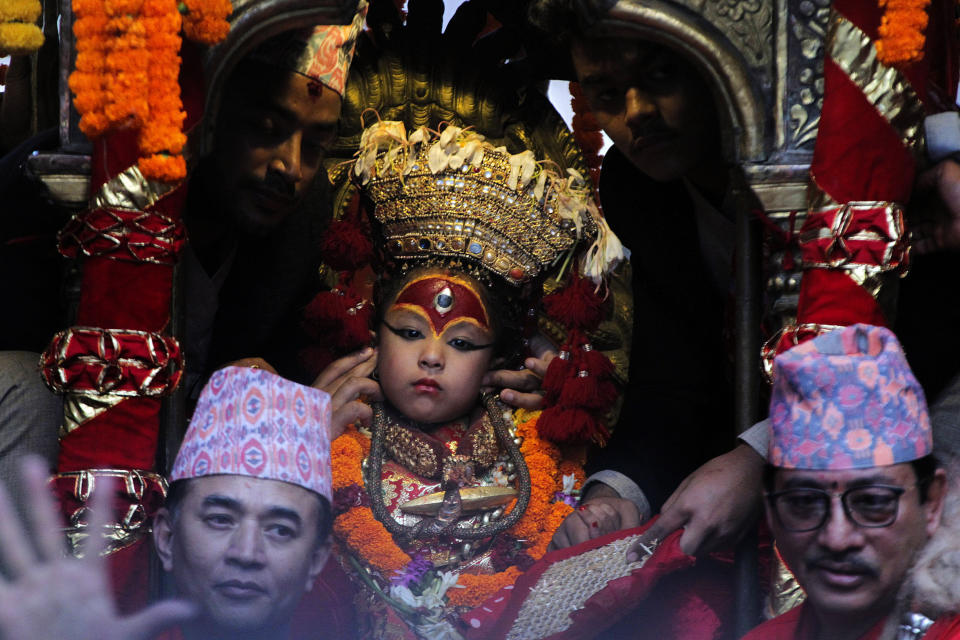 A priest covers the ears of living goddess Kumari as soldiers fire a gun as a part of rituals during Indra Jatra festival, an eight-day festival that honors Indra, the Hindu god of rain, in Kathmandu, Nepal, Friday, Sept. 13, 2019. The girl child revered as the Living Goddess Kumari is pulled around Kathmandu in a wooden chariot, families gather for feasts and at shrines to light incense for the dead, and men and boys in colorful masks and gowns representing Hindu deities dance to the beat of traditional music and devotees' drums, drawing tens of thousands of spectators to the city's old streets. (AP Photo/Niranjan Shrestha)