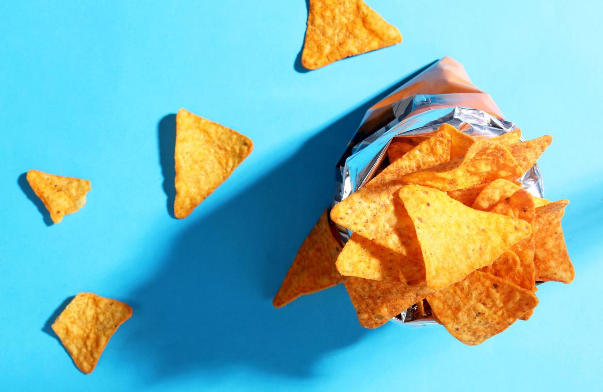 Opened bag of Doritos with a blue background with a few pieces scattered, view from top looking down