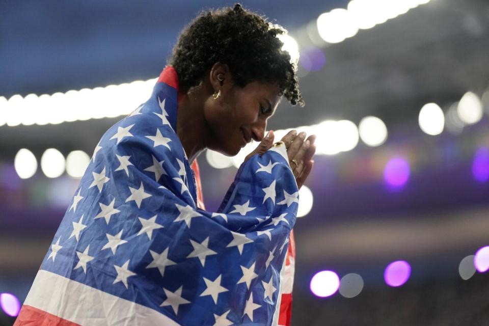 Anna Cockrell of the U.S. puts her hands together while wearing a U.S. flag under bright lights.