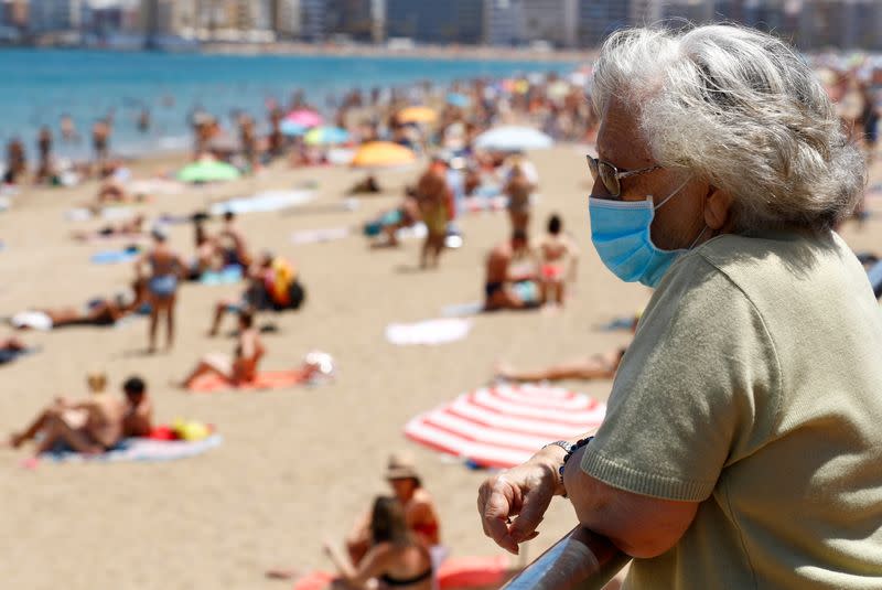 FILE PHOTO: A woman wearing a face mask watches people sunbathing on the Las Canteras beach