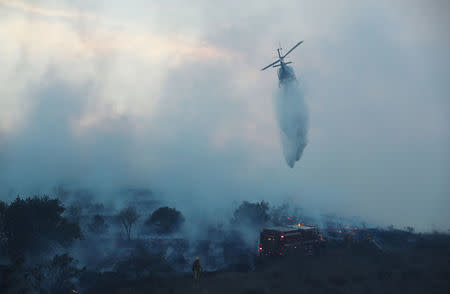 A firefighting helicopter makes a water drop on the Lilac Fire, a fast moving wildfire in Bonsall, California, U.S., December 7, 2017. REUTERS/Mike Blake