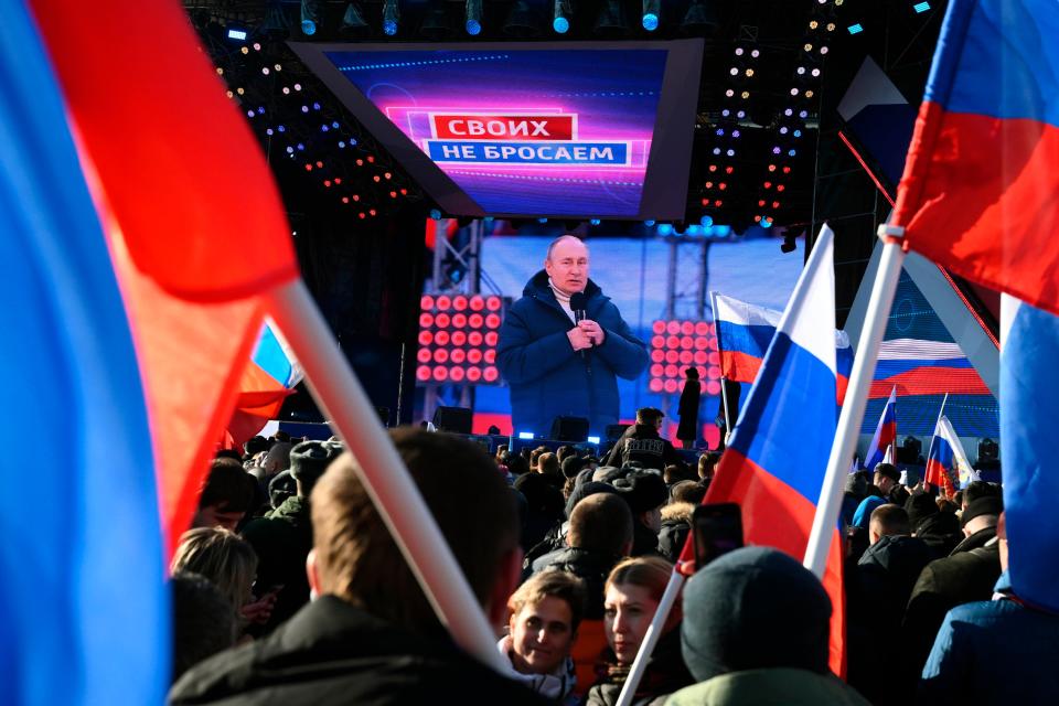 Russian President Vladimir Putin is seen on a big screen as he delivers his speech at the concert marking the eighth anniversary of the referendum on the state status of Crimea and Sevastopol and its reunification with Russia, in Moscow, Russia, Friday, March 18, 2022, with the words reading "We don't abandon our own" projected.