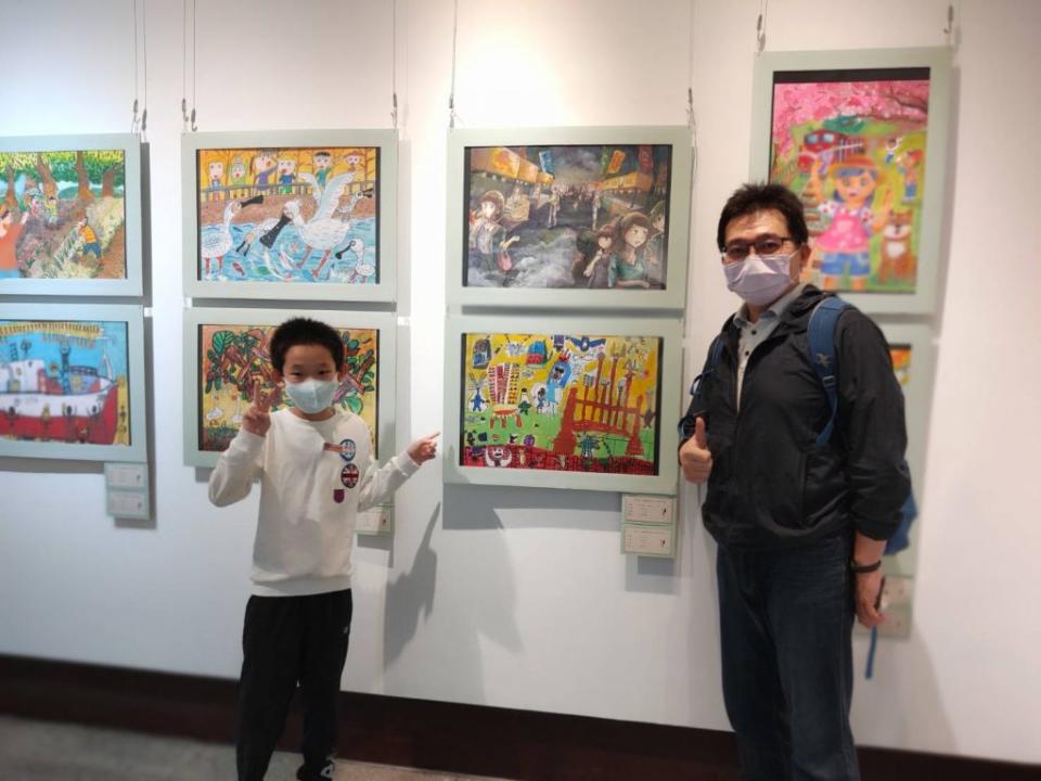 新北市小學生傅士維在爸爸的帶領下，到畫展與自已的作品「兵器」合影。（記者陳威穎、王柏倫攝）