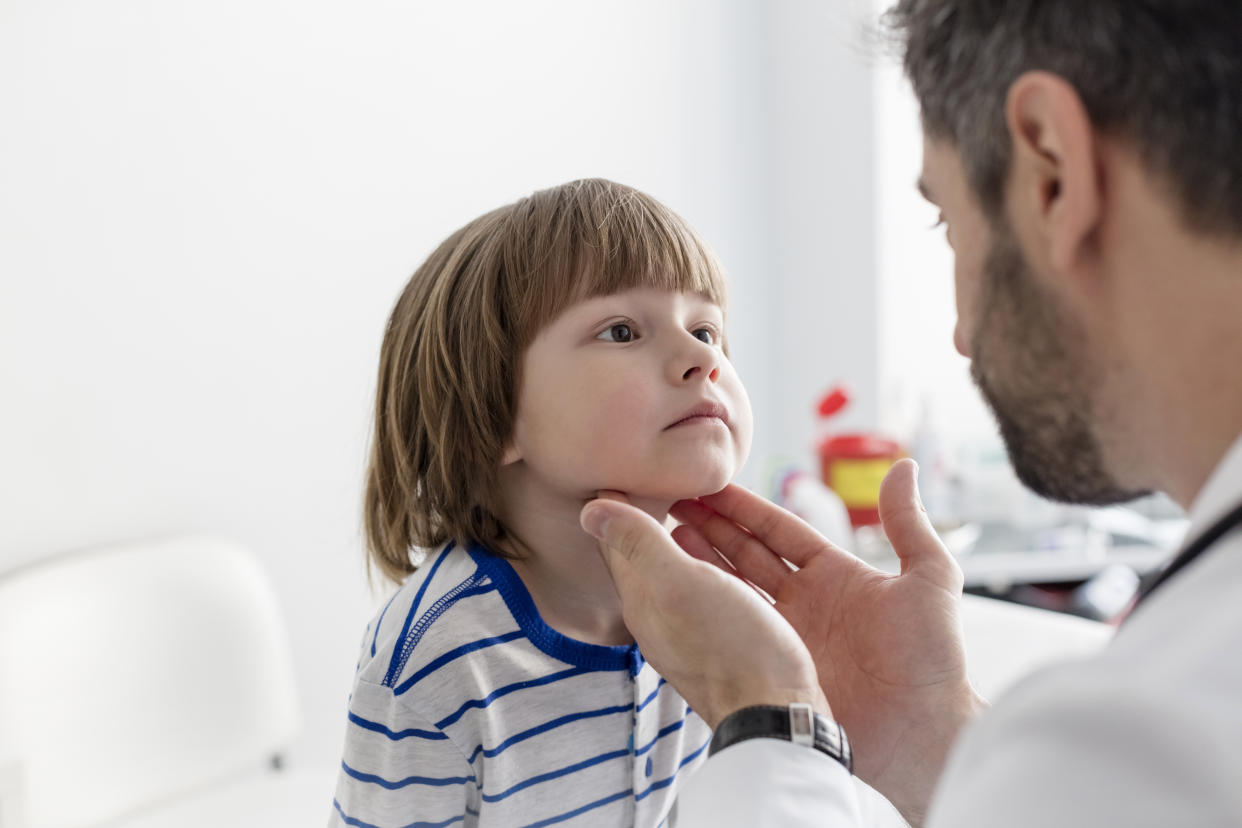 A young child sitting in a chair looks up at a doctor during an exam.