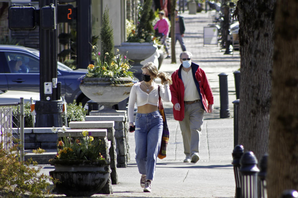 Residents wearing masks walk in downtown Lake Oswego, Ore., on Sunday, April 11, 2021. Tens of thousands of Oregon residents are angry about a proposal to make permanent an emergency rule that requires masks and social distancing in the state's businesses and schools to prevent the spread of COVID-19. Opponents worry about government overreach and fear that state officials won't remove the mask requirements for businesses even after threat of the virus has receded if the emergency rule becomes permanent. (AP Photo/Gillian Flaccus)