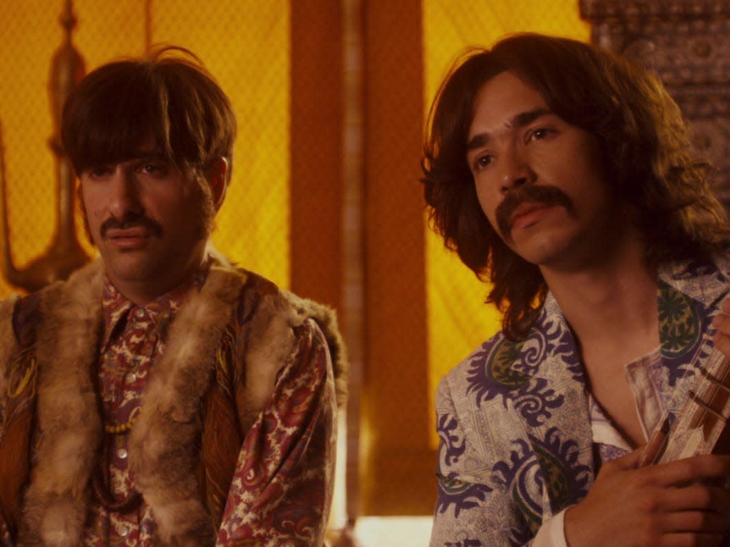 jason schwartzman and justin long as ringo starr and george harrison in walk hard. they're wearing eccentric clothes, and justin is holding a sitar