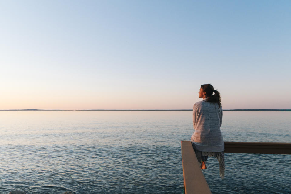 A woman sitting on a ledge over the ocean looking out